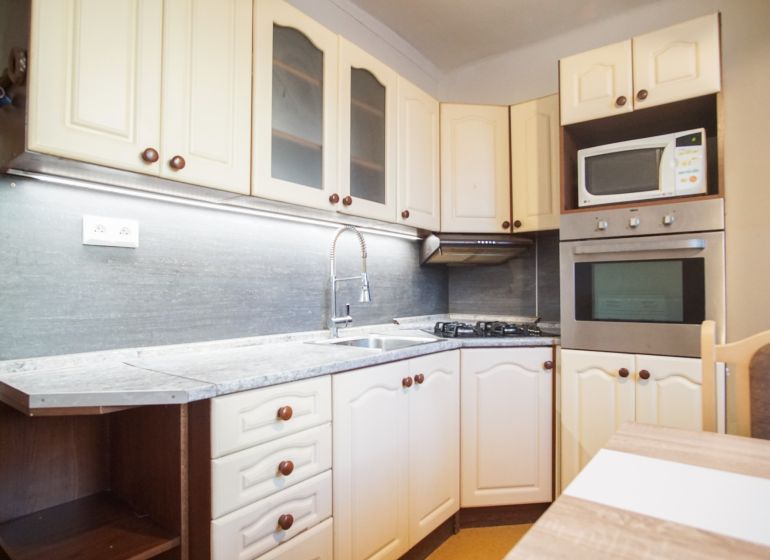 Küche in einer 2-Zimmer-Wohnung mit weißen Schränken und eingebauten Geräten.