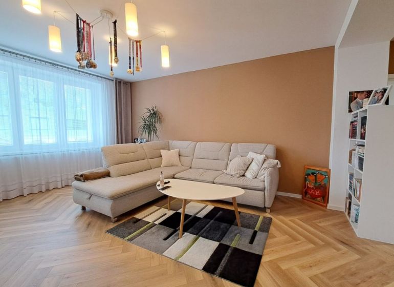 Wohnzimmer in einer 3-Zimmer-Wohnung mit einem weißen Sofa und einem Boden in Holzoptik.