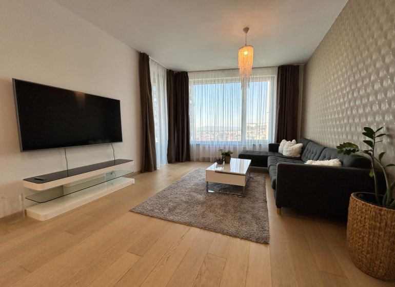 Wohnzimmer in einer 2-Zimmer-Wohnung mit Holzboden, großem Fenster und Fernseher.