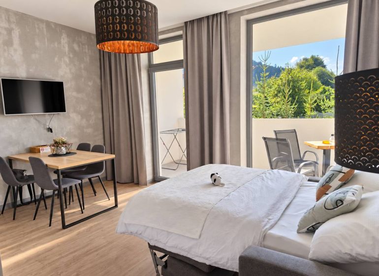 Ein Zimmer in einer 2-Zimmer-Wohnung mit einem Holzboden, einem Esstisch und einem Bett.