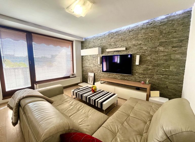 Wohnzimmer in einer 3-Zimmer-Wohnung mit Ledersofa, Steinwand und Holzboden.