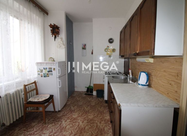 Küche in einer 2-Zimmer-Wohnung mit Kühlschrank, Holzboden, hellem Vorhang.
