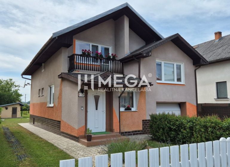 Ein Einfamilienhaus in Lackovce mit Balkon, umgebender Vegetation und einem weißen Zaun.