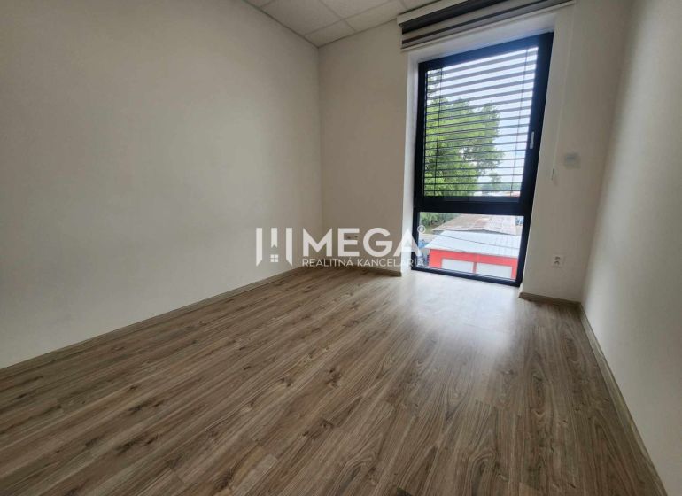 Ein Büro mit einem Boden in Holzoptik und einem großen Fenster, schlichtes Interieur.