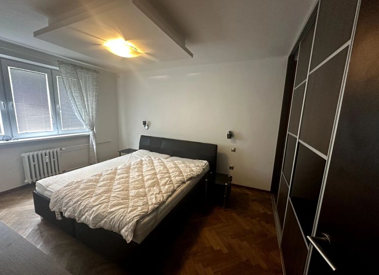 Schlafzimmer in einer 2-Zimmer-Wohnung mit Bett, Kleiderschrank und Boden in Holzoptik.