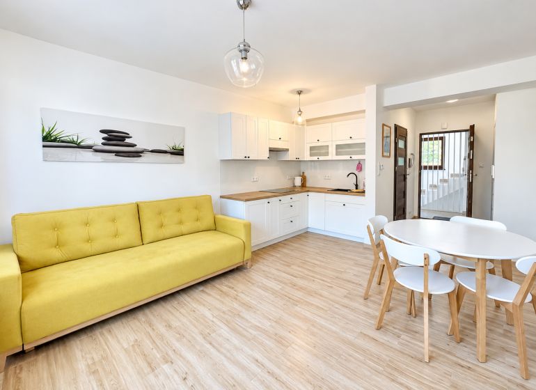 Wohnzimmer in einer Einzimmerwohnung mit Holzboden und gelbem Sofa.