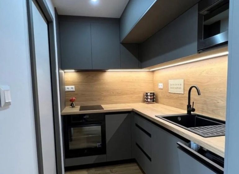 Küche in einer Einzimmerwohnung mit Holzdekorboden, graue Schränke, schwarzes Spülbecken.