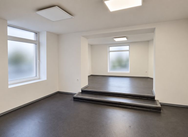 Ein helles Büro mit einem dunklen Boden in Holzoptik und einer Treppe im Raum.