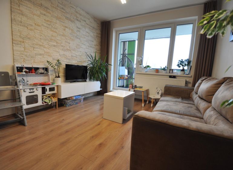 Wohnzimmer in einer 3-Zimmer-Wohnung mit Holzboden und Steinverkleidung an der Wand.