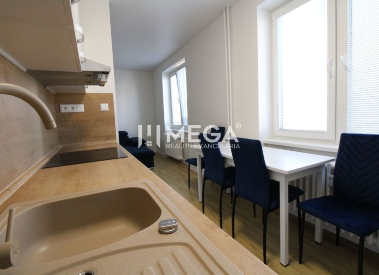 Küche in einer 2-Zimmer-Wohnung mit weißen Möbeln, blauen Stühlen und einem Boden in Holzoptik.