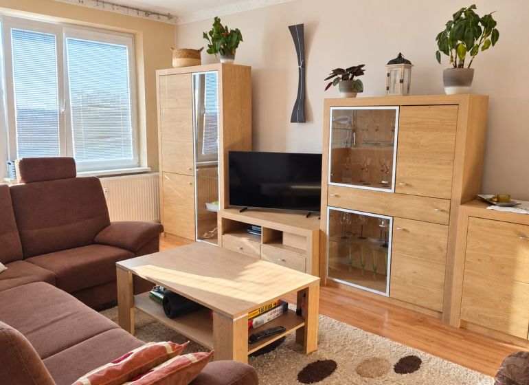Wohnzimmer mit braunem Sofa, Holzmöbeln und Boden mit Holzdekor.