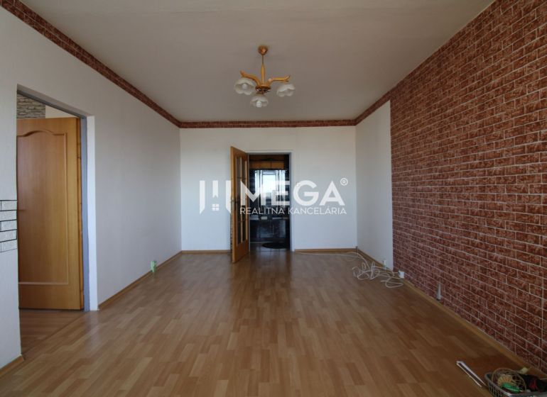 Ein Zimmer in einer 3-Zimmer-Wohnung mit einem Holzboden und einer Wand im Ziegelmuster.