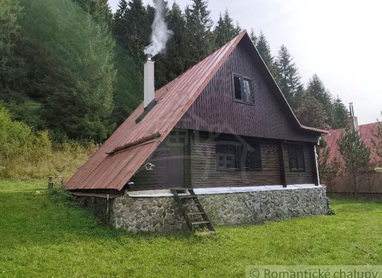 Eine Hütte in Rajecká Lesná, umgeben von Wald, mit Rauch aus dem Schornstein.