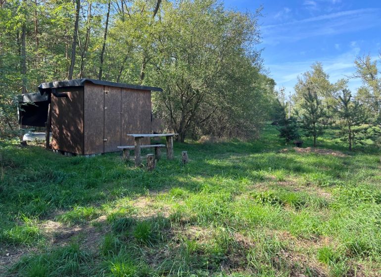 Gärten in Kopčany mit einem Holzunterstand, umgeben von Bäumen und grünem Gras.