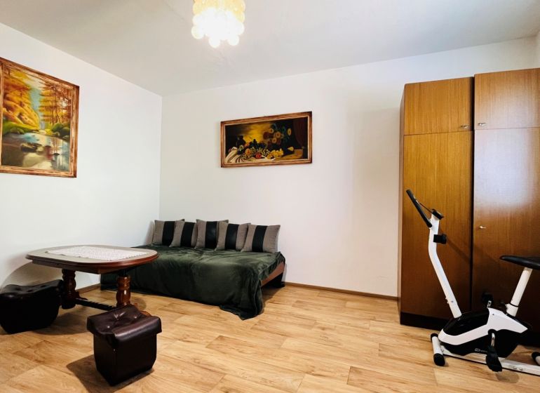 Ein Zimmer in einer 3-Zimmer-Wohnung mit einem Sofa, einem Tisch und einem Boden in Holzoptik.
