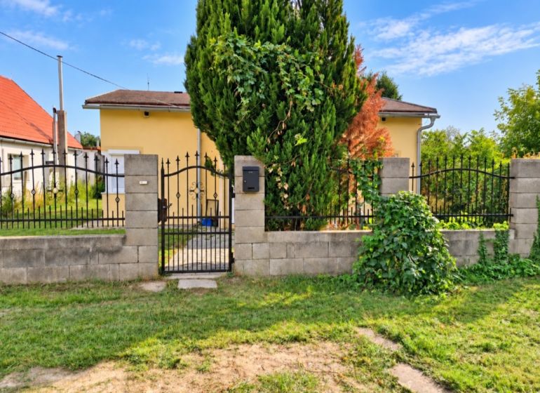 Ein Einfamilienhaus in Martovce mit einem Vorgarten und einem Metalltor, umgeben von einer Hecke.