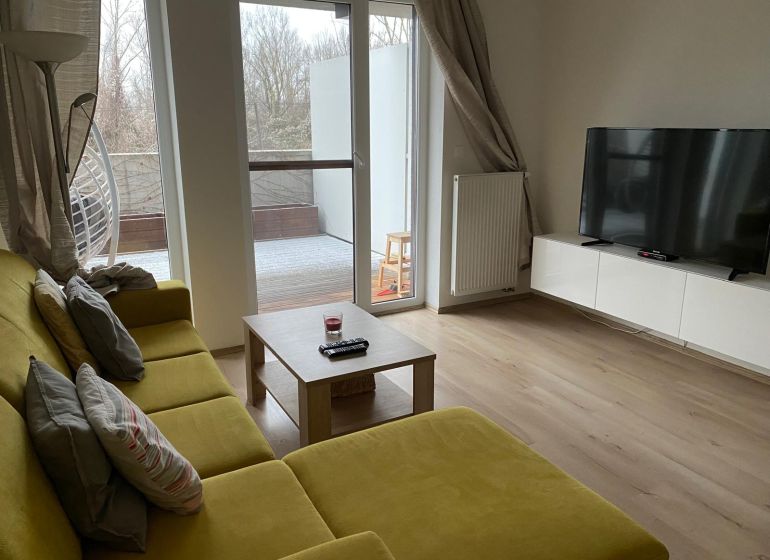 Wohnzimmer in einer Zweizimmerwohnung mit Sofa und Fernseher; Boden mit Holzdekor.