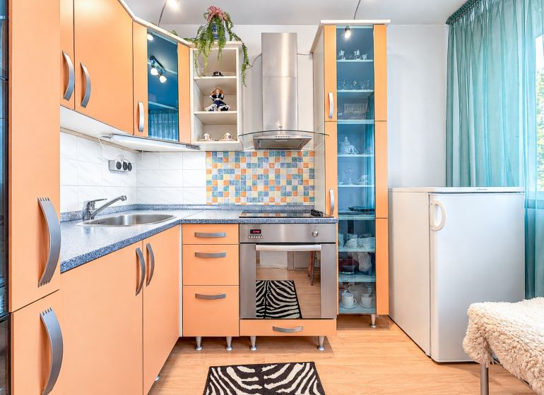Küche in einer Einzimmerwohnung mit bunten Schränken, Fliesenmosaik und Bodenbelag in Holzoptik.