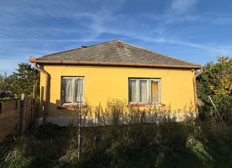 Gelbes Einfamilienhaus in Komárno mit Zaun und Garten unter blauem Himmel.