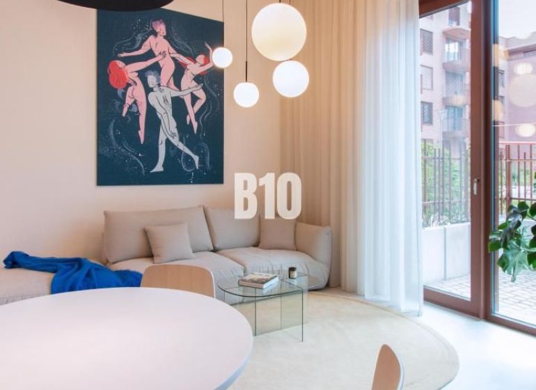 Wohnbereich mit weißen Möbeln, rundem Tisch und Kunst in einer 2-Zimmer-Wohnung.