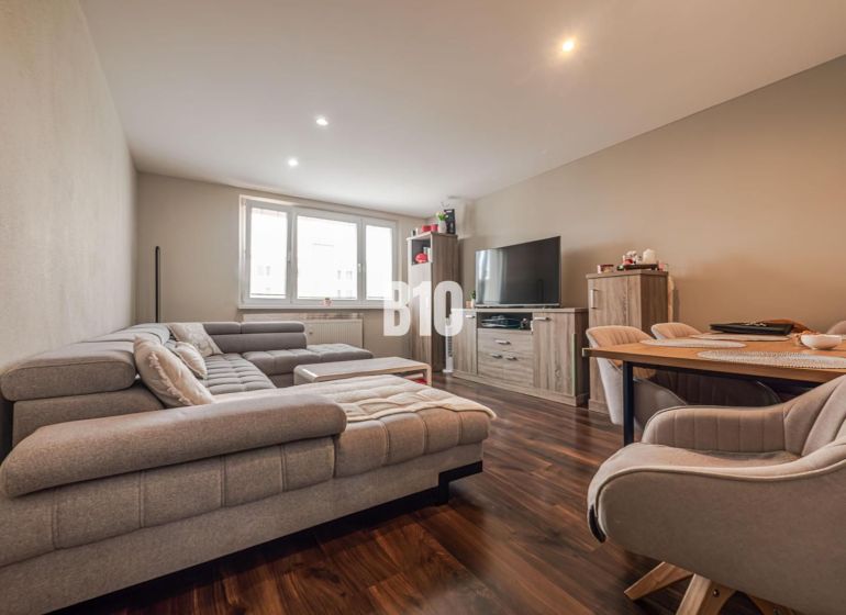 Wohnzimmer in einer 3-Zimmer-Wohnung mit einem bequemen Sofa und einem Boden in Holzoptik.