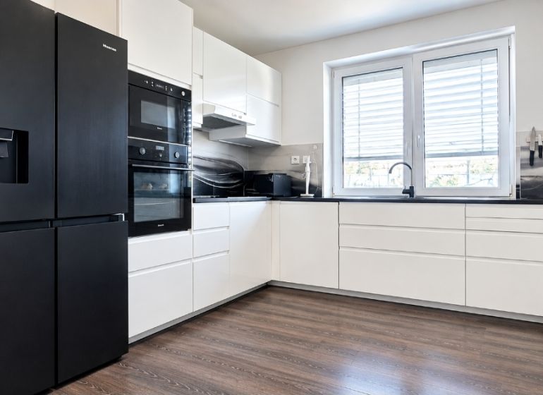 Küchenzeile mit schwarzen Geräten und einem Boden in Holzoptik in einem Einfamilienhaus.