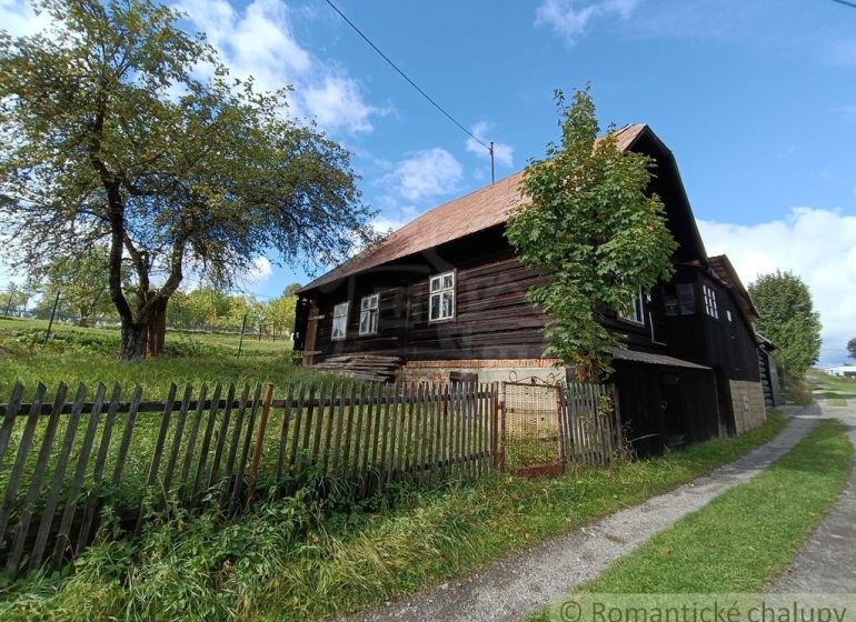 Eine Holzhütte in Staškov, umgeben von Gras und Bäumen hinter einem Zaun.