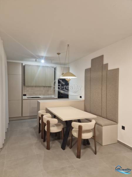 Esszimmer in einer Ferienwohnung mit Küche, hellen Stühlen und grauen Wandpaneelen.