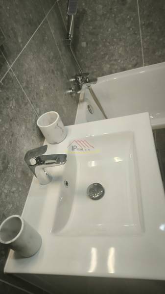 Waschbecken und Badewanne im Badezimmer eines Einzimmerapartments mit grauen Fliesen.