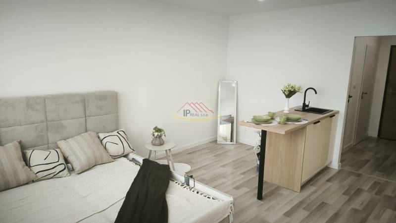 Garçonniere mit Bett, Spiegel, Küchenzeile und hellem Boden.