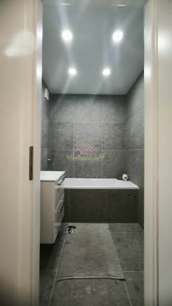 Ein Badezimmer in einem Studio-Apartment mit Wänden, die mit dunklen Fliesen verkleidet sind, und einer Badewanne.