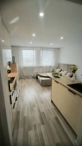Einzimmerwohnung mit Kochnische, hellem Boden und bequemer Sitzgelegenheit.