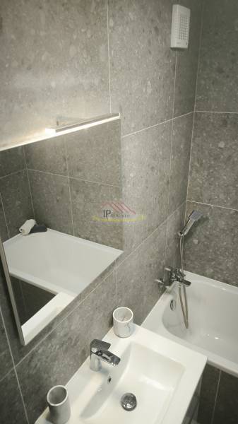 Badezimmer mit Badewanne und Waschbecken in einer Einzimmerwohnung mit grauen Fliesen.