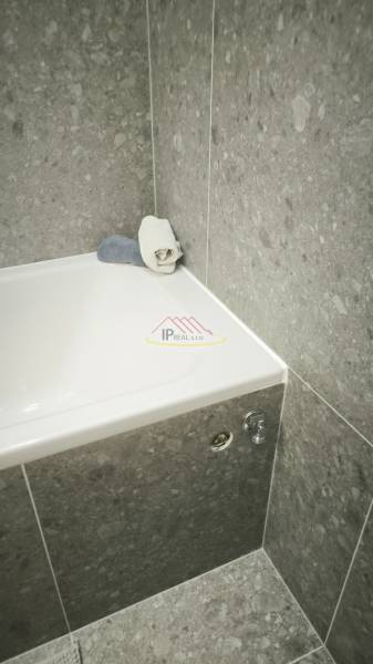 Badezimmer mit Badewanne und grauen Fliesen, geeignet für ein Studio-Apartment.
