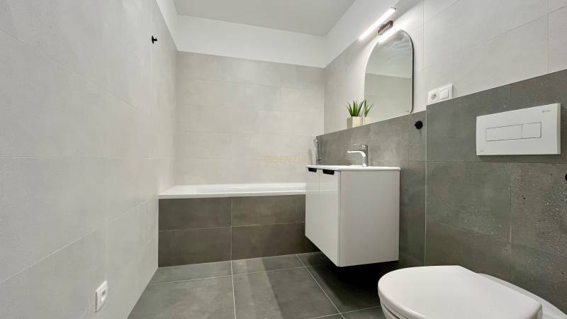 Badezimmer mit Badewanne, Waschbecken, Spiegel und Toilette in einer 2-Zimmer-Wohnung.