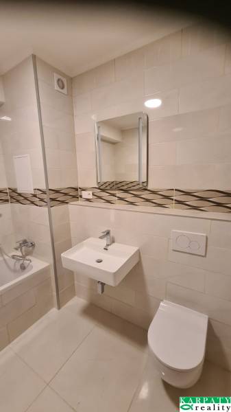 Badezimmer in einer Einzimmerwohnung mit Badewanne, Waschbecken und Toilette, Fliesen mit dekorativem Streifen.