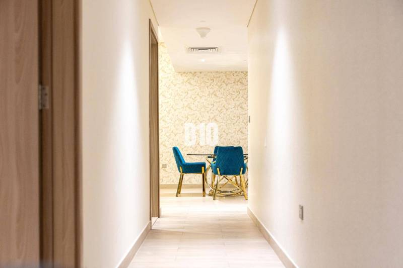 Der Flur führt in ein Zimmer mit blauen Stühlen und einer gemusterten Wand in einer 3-Zimmer-Wohnung.