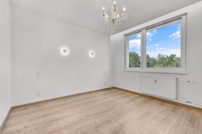Ein leerer Raum mit Holzboden, Kronleuchter und großem Fenster, 4-Zimmer-Wohnung.