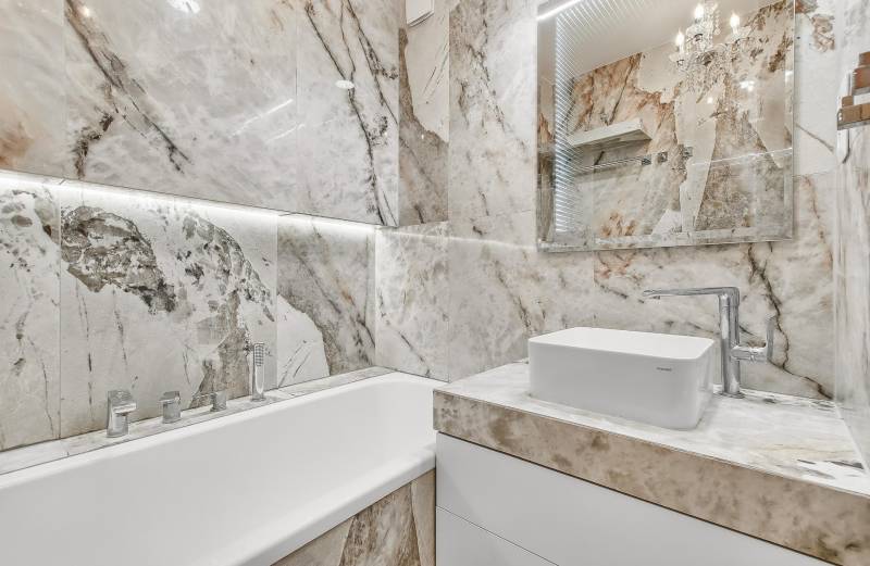 Ein Badezimmer in einer 4-Zimmer-Wohnung mit einer Badewanne und einem Waschbecken, umgeben von Marmorfliesen.