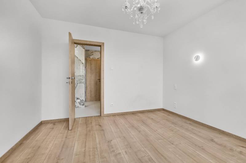 Ein leerer Raum mit Holzboden und einem Kronleuchter in einer Vierzimmerwohnung.