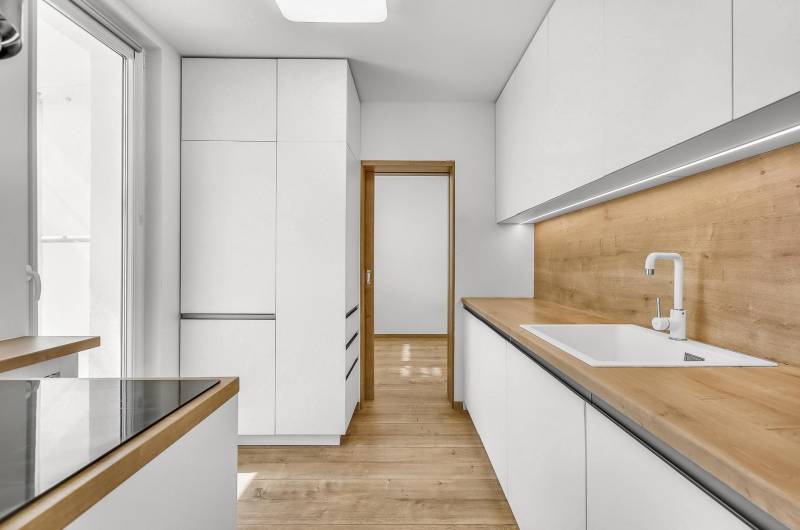 Küche in einer 4-Zimmer-Wohnung mit weißen Schränken und einer Holzarbeitsplatte.