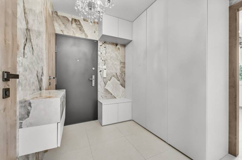 Diele einer 4-Zimmer-Wohnung mit weißen Möbeln, strukturierten Wänden und einem Kronleuchter.