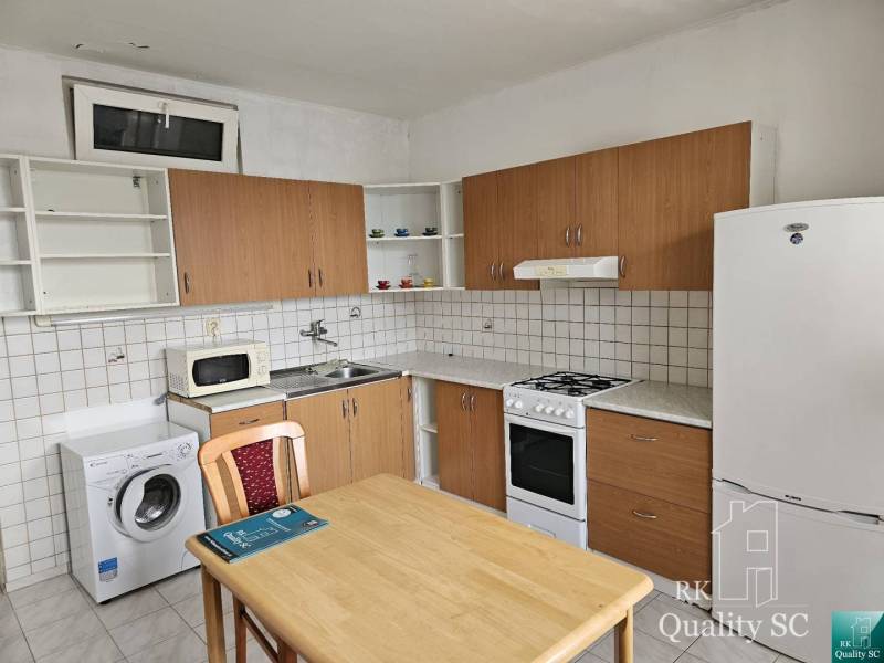 Küchenbereich einer 2-Zimmer-Wohnung mit Kühlschrank, Waschmaschine und Herd, Holztisch mit Stuhl.
