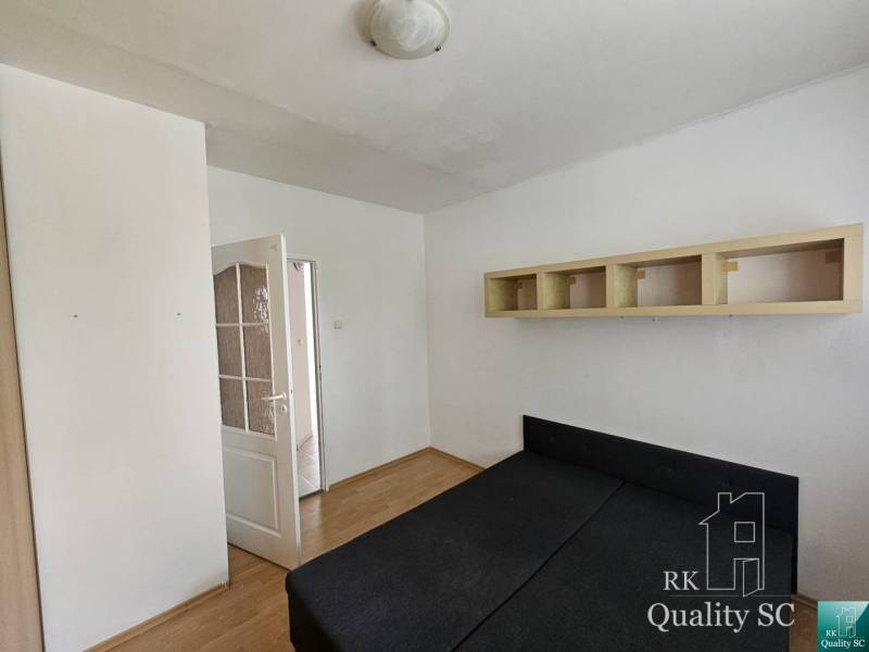 Schlafzimmer in einer 2-Zimmer-Wohnung mit Bett, Schrank und offener Tür, die in den Flur führt.