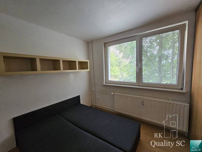 Schlafzimmer in einer 2-Zimmer-Wohnung mit Bett, Regal und Fenster mit Blick auf Grünflächen.