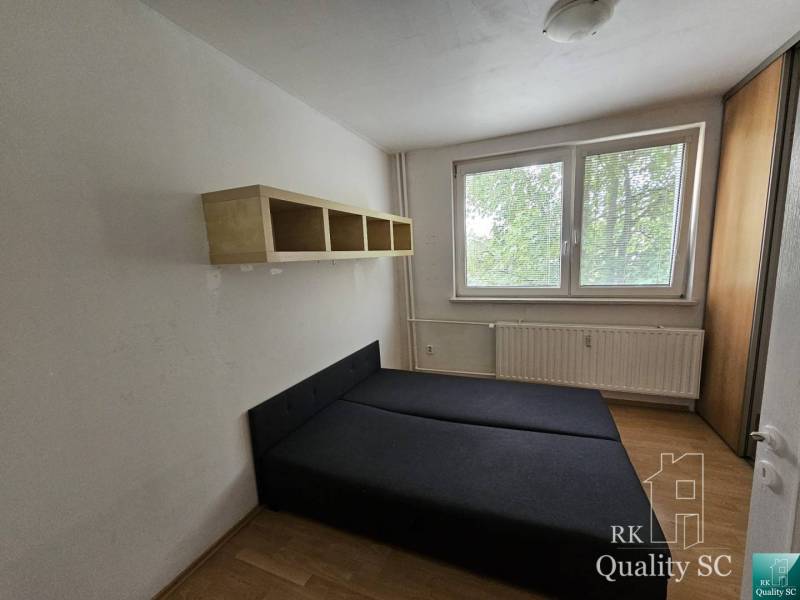 Schlafzimmer mit Bett und Regal in einer 2-Zimmer-Wohnung. Fenster mit Blick auf das Grün.