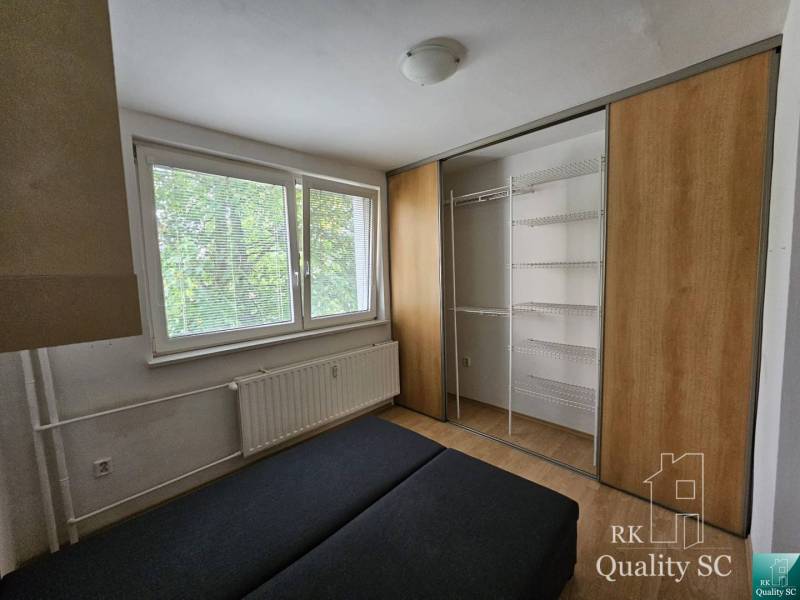 Schlafzimmer in einer 2-Zimmer-Wohnung mit einem großen Einbauschrank und einem Heizkörper unter dem Fenster.