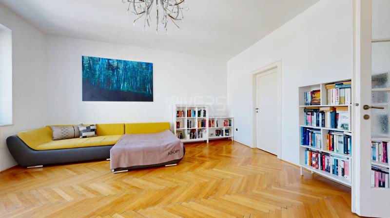 Wohnzimmer in einer 3-Zimmer-Wohnung mit Sofa, Bücherregal, Bild und Holzboden.