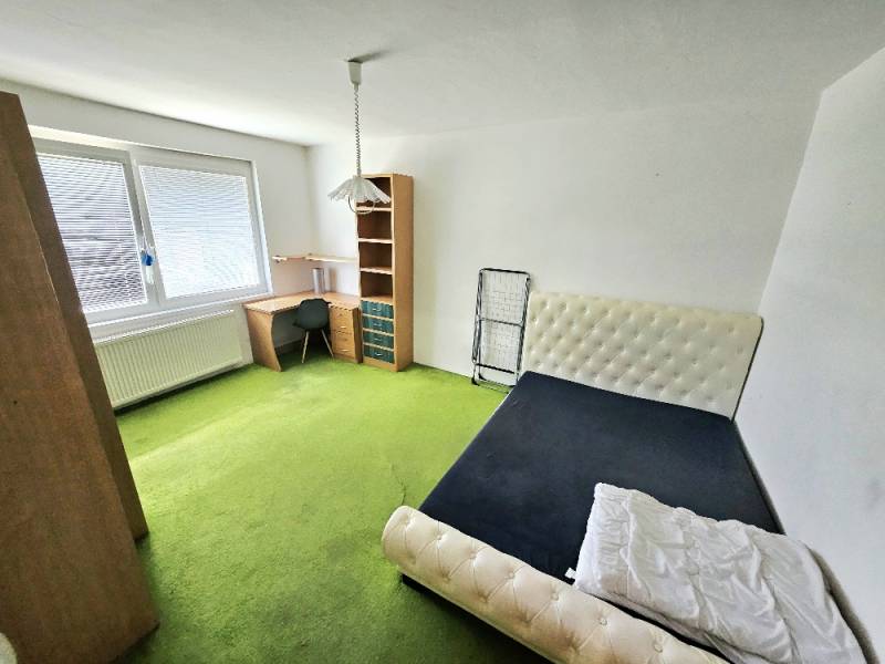 Ein Zimmer in einer 3-Zimmer-Wohnung mit einem Bett, einem Tisch und einem grünen Teppich.