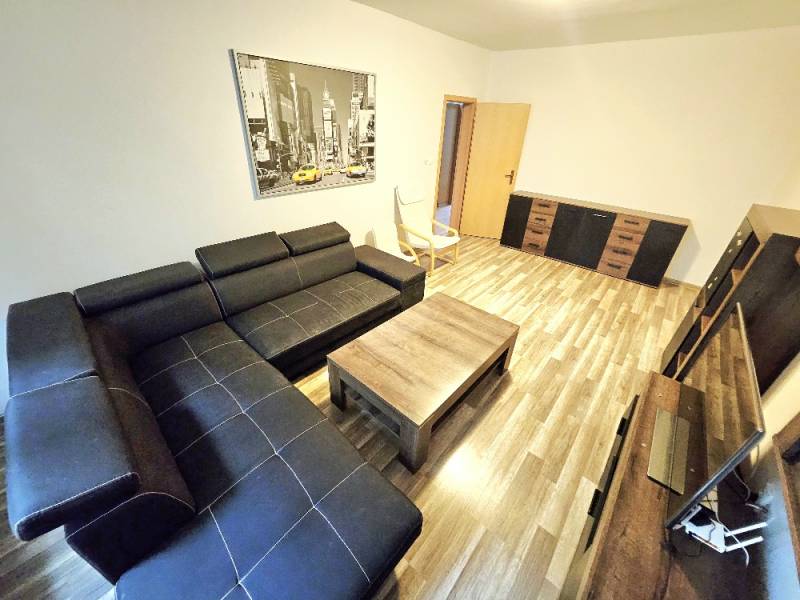 Wohnzimmer in einer 3-Zimmer-Wohnung mit schwarzem Sofa und Holzmöbeln.